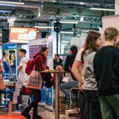 Menschen stehen an Ständen auf einer Messe, einige sprechen miteinander und andere schauen auf Informationen.