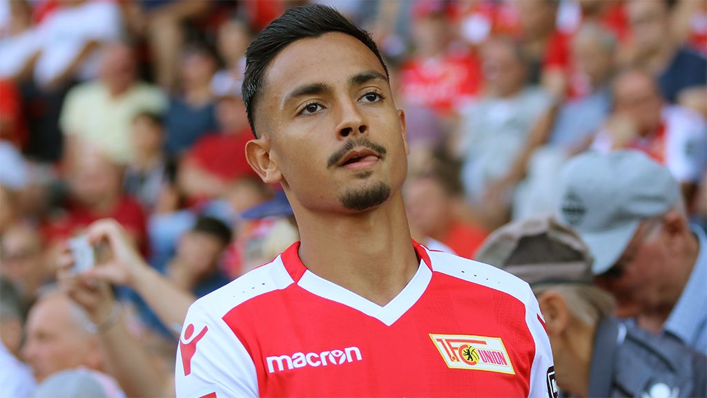 A football player with short hair and a focused expression is wearing a jersey with a red and white design.