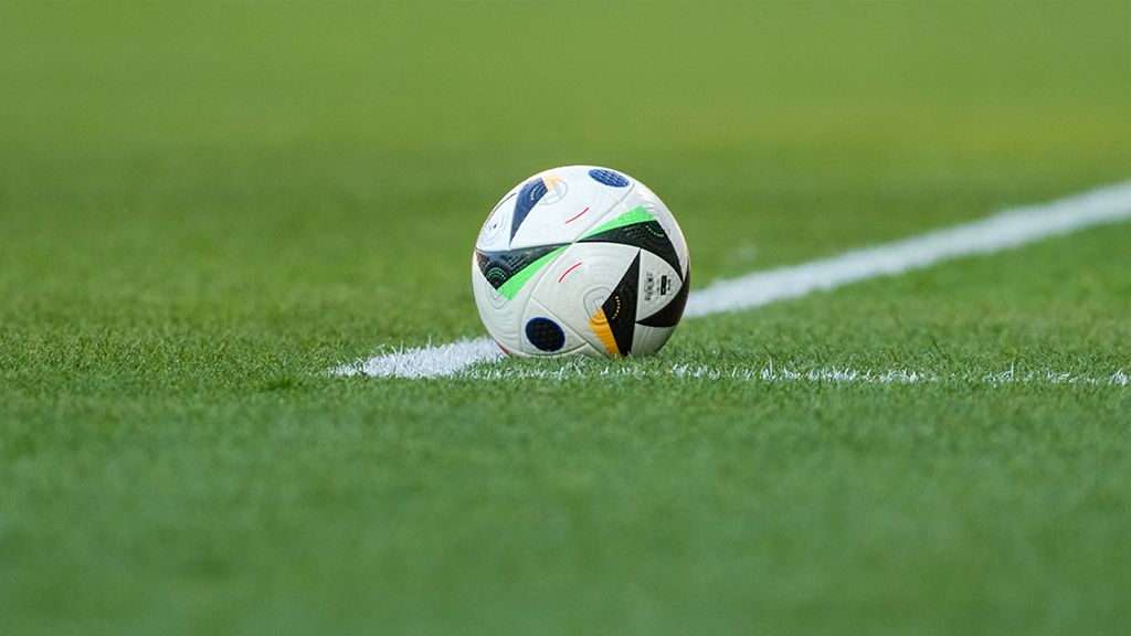 Ein Fußball liegt am Rand eines Rasenfeldes, teilweise auf der wei ßen Linienmarkierung.