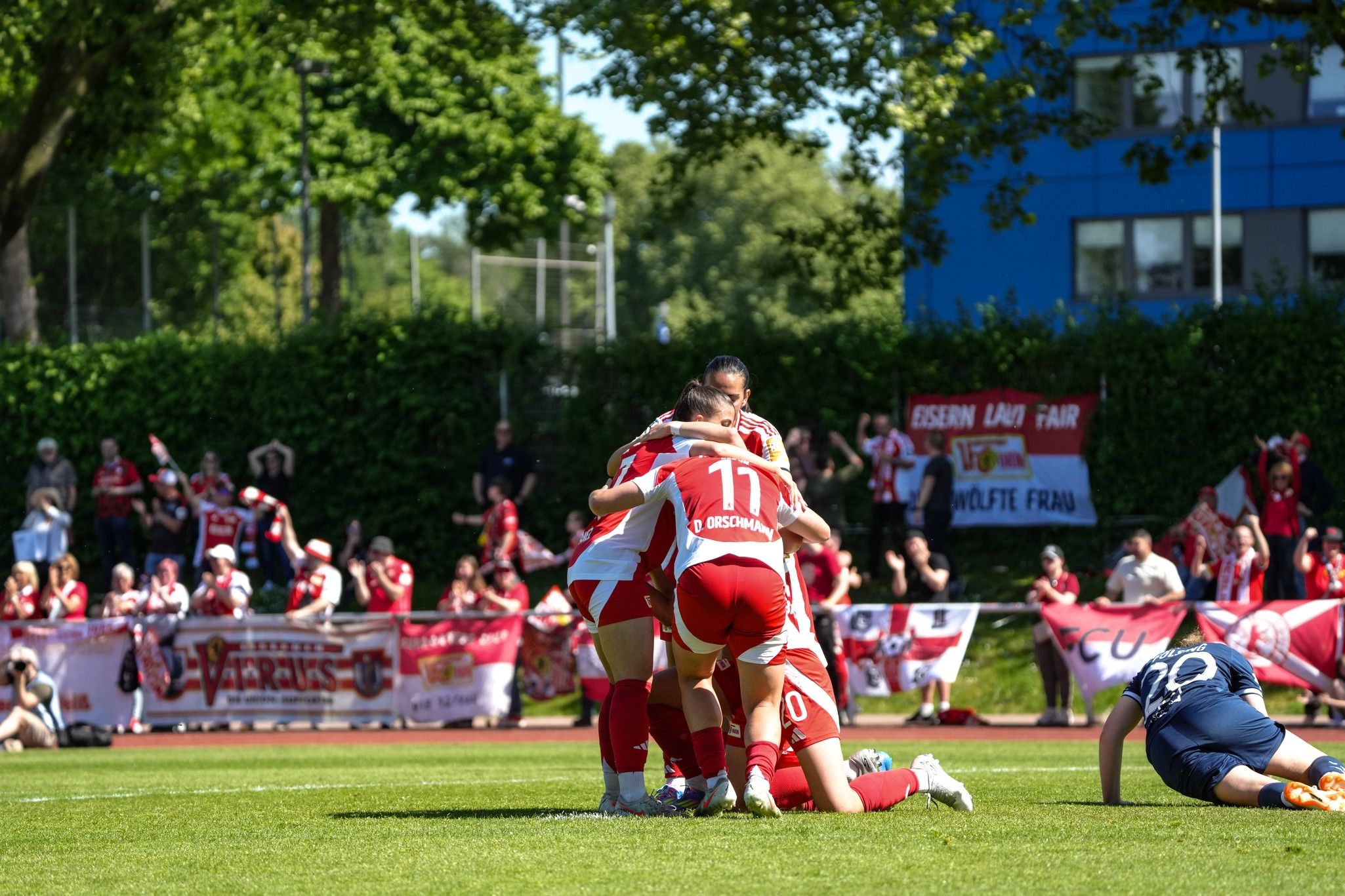 Los jugadores de un equipo de fútbol celebran juntos en la hierba, mientras los aficionados al fondo animan con colores rojo y blanco.