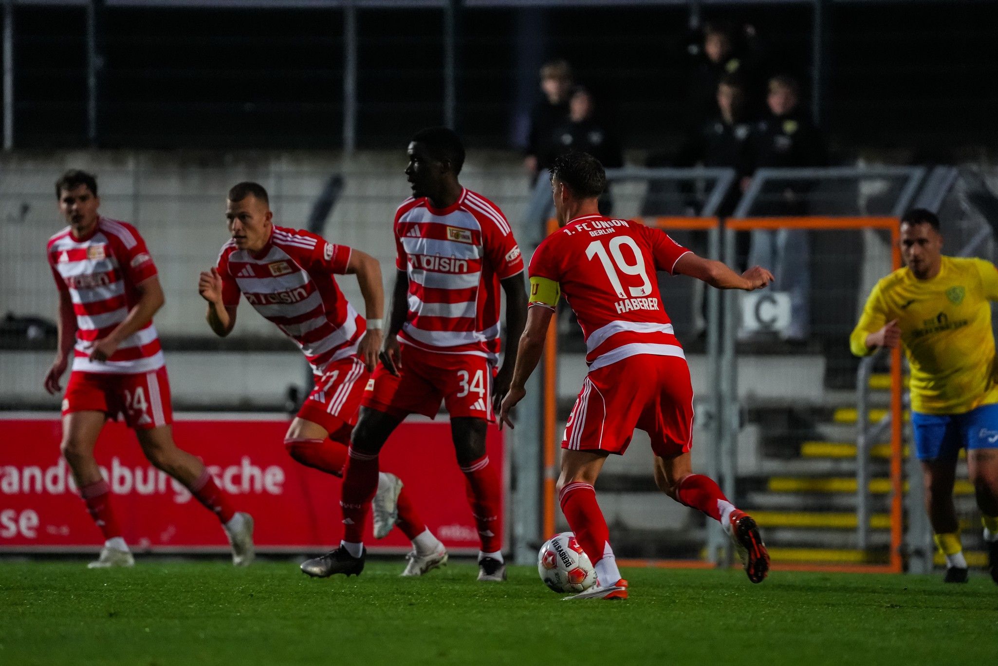 Spielszene mit fünf Fußballspielern in rot-weißen Trikots auf dem Platz, einer Spieler mit der Nummer 19 führt den Ball.