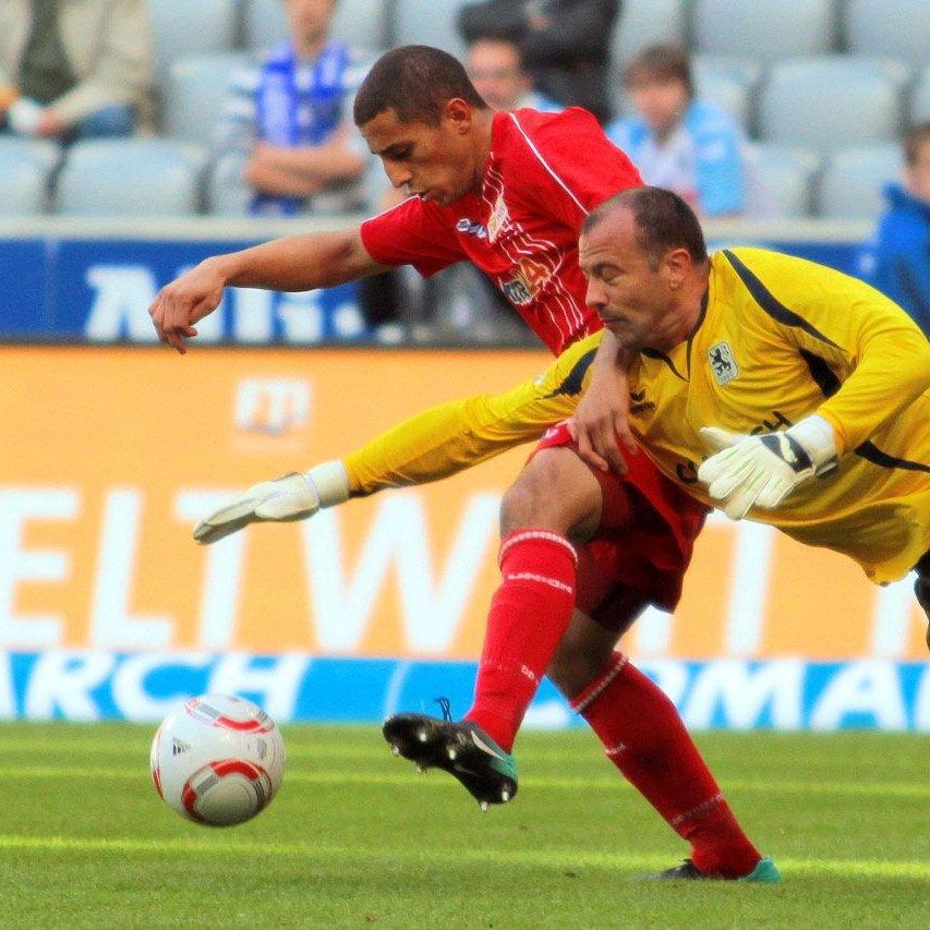 Spielszene im Fußball: Ein Spieler schießt auf das Tor, während der Torwart versucht, den Ball abzuwehren.