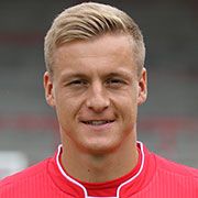 Ein junger Mann mit blonden Haaren und sportlicher Kleidung lächelt in die Kamera.