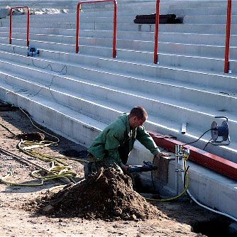 Ein Arbeiter steht an einer Baustelle und bearbeitet den Boden neben einer Reihe von betonierten Stufen.
