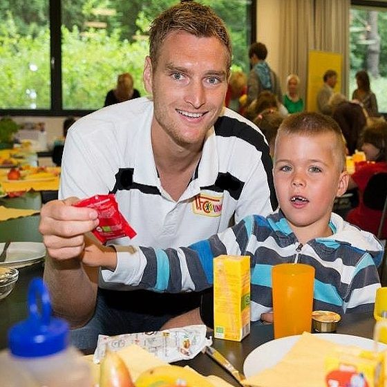 Ein Mann und ein Junge sitzen an einem Tisch mit Essen und Getränken, lächeln und halten eine kleine Packung in der Hand.