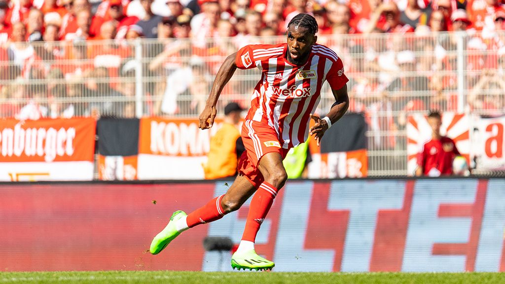 Ein Fußballspieler in roter und weißer Uniform sprintet über das Spielfeld vor jubelnden Fans.