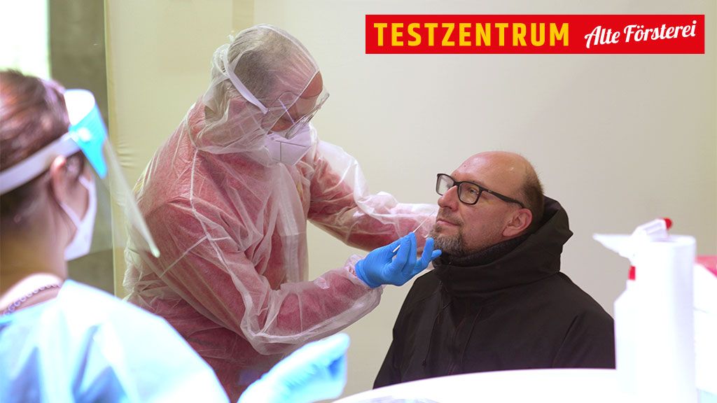 Man at the testing center receives a swab from a medical professional, both wearing protective equipment.