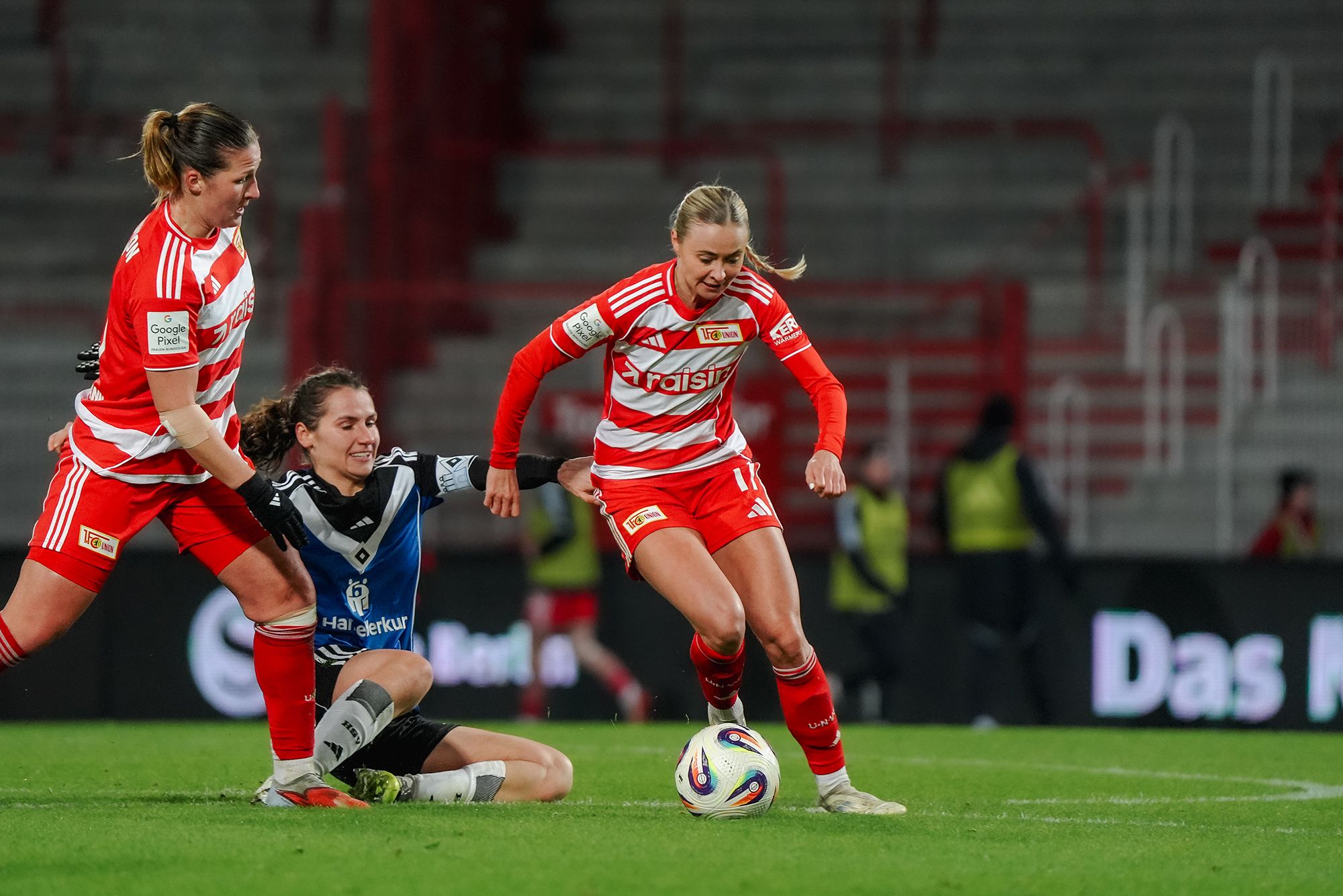 Zwei Fußballspielerinnen von Union Berlin und eine Torhüterin im Wettkampf um den Ball auf dem Spielfeld.
