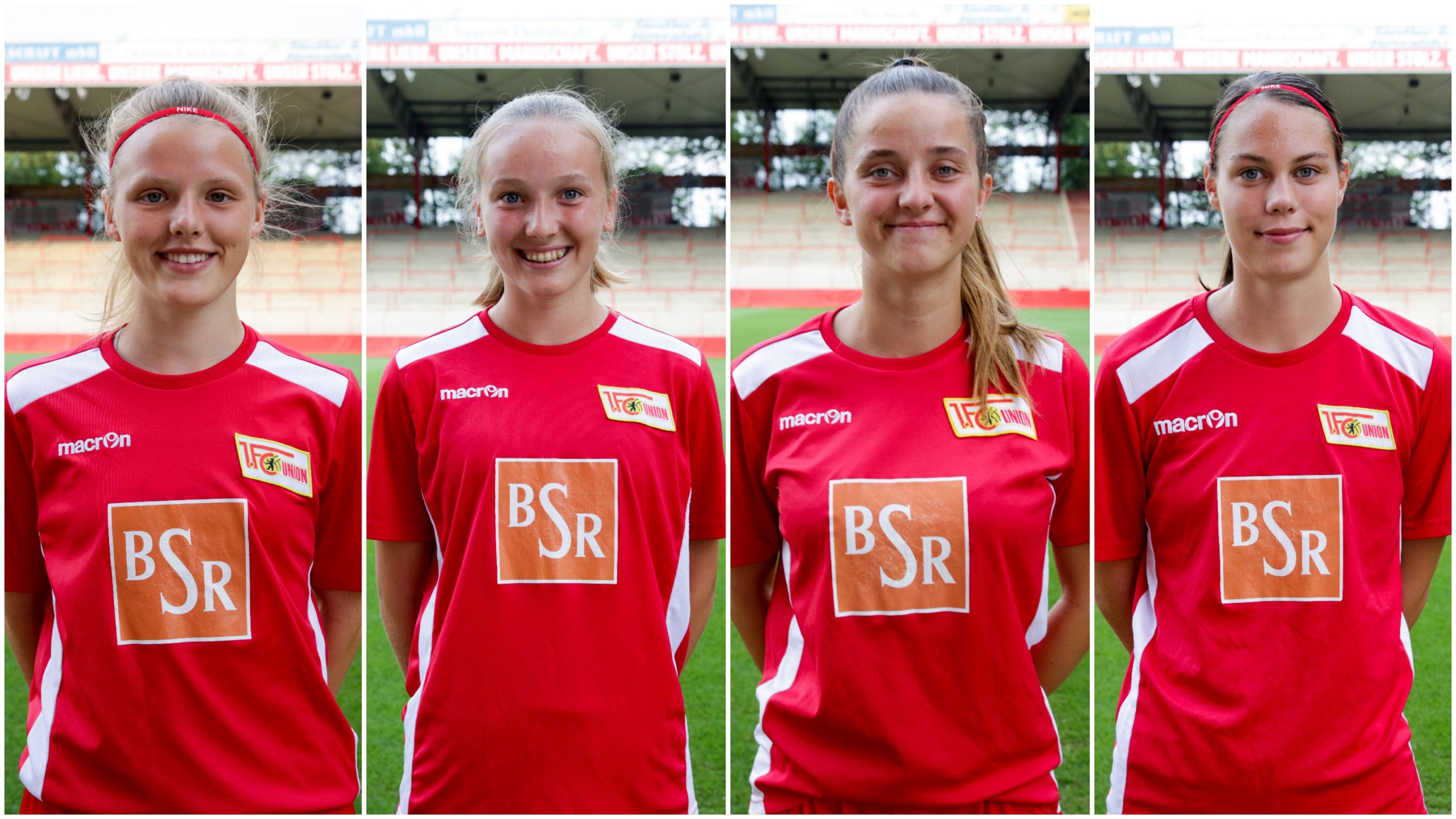 Vier junge Fußballspielerinnen in roten Trikots posieren lächelnd vor einer Sportstätte.