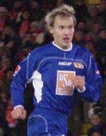 Ein Fußballspieler in blauer Mannschaftsbekleidung läuft auf dem Platz, umgeben von Zuschauern im Hintergrund.