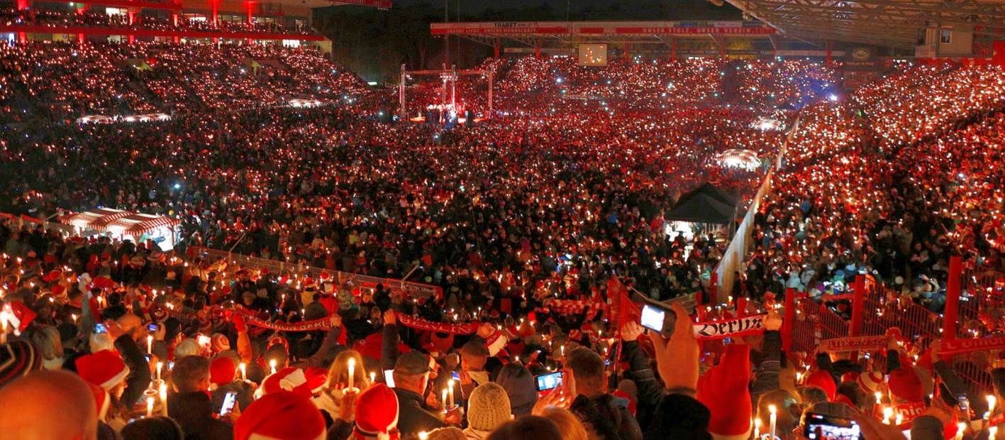 Ein großes Publikum in einem Stadion, das bei einem Event Kerzen hält und in festlicher Atmosphäre leuchtet.