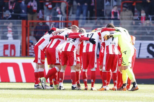 A group of football players in red and white jerseys hugs in a circle, ready for the game.
