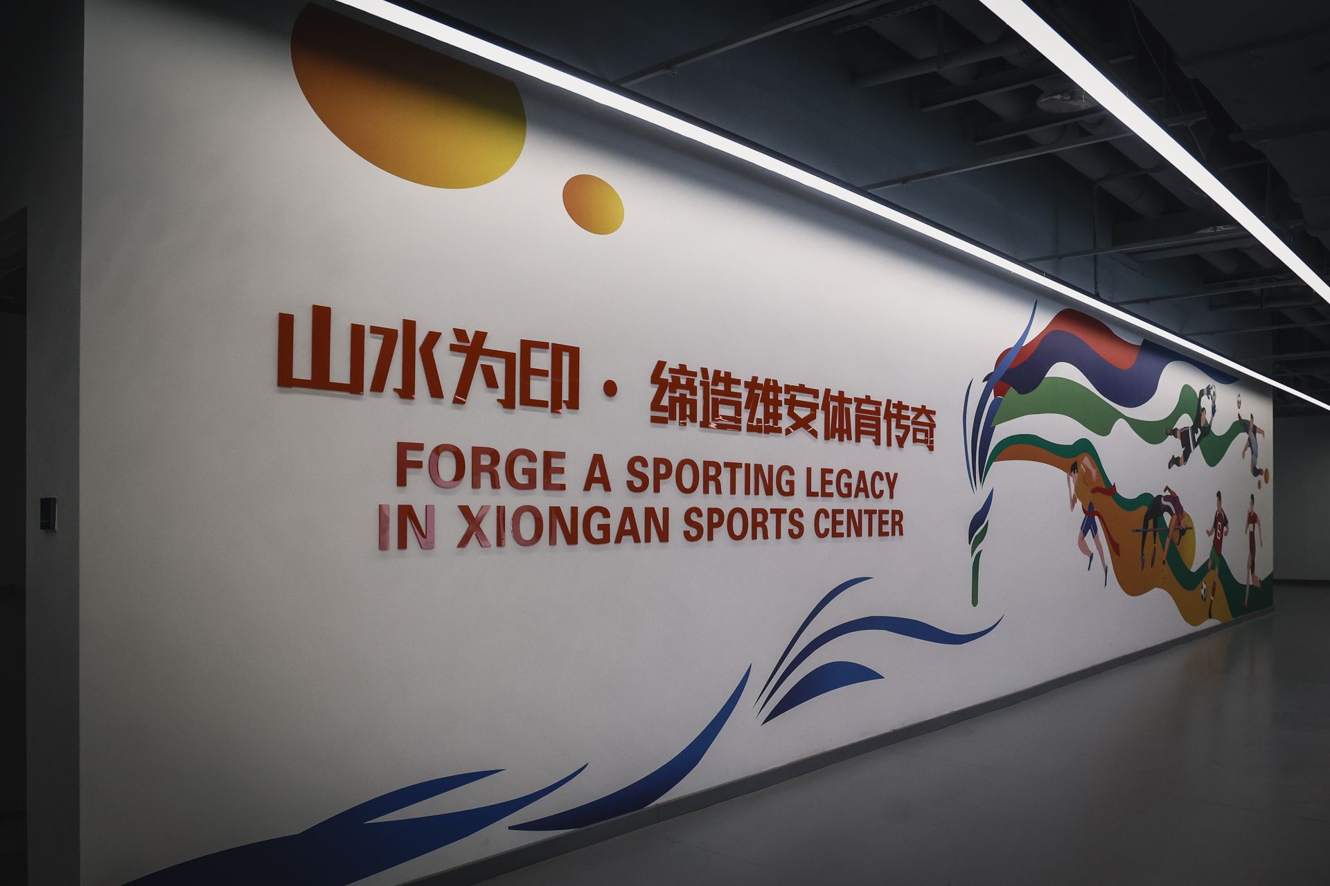 Wandmalerei im Xiong'an Sports Center mit dem Schriftzug „Forge a Sporting Legacy“ und farbigen Sportmotiven.