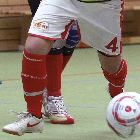 Fußballspieler in rot-weißer Ausrüstung mit der Nummer 4, der einen Ball auf einem Sportplatz kickt.