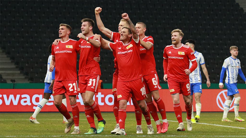Football players in red jerseys celebrate a goal on the field.