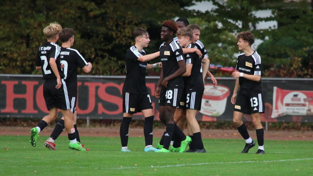 Junge Fußballspieler in schwarzen Trikots feiern ein Tor auf einem Rasenplatz.