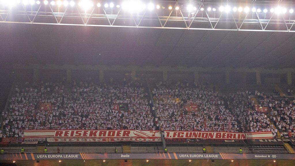 Fans des 1. FC Union Berlin in einem Stadion, gekleidet in Weiß und Rot, mit einem großen Banner.