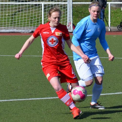 Zwei Fußballspielerinnen in Aktion auf dem Spielfeld; eine in rotem Trikot, die andere in hellblauem Trikot.