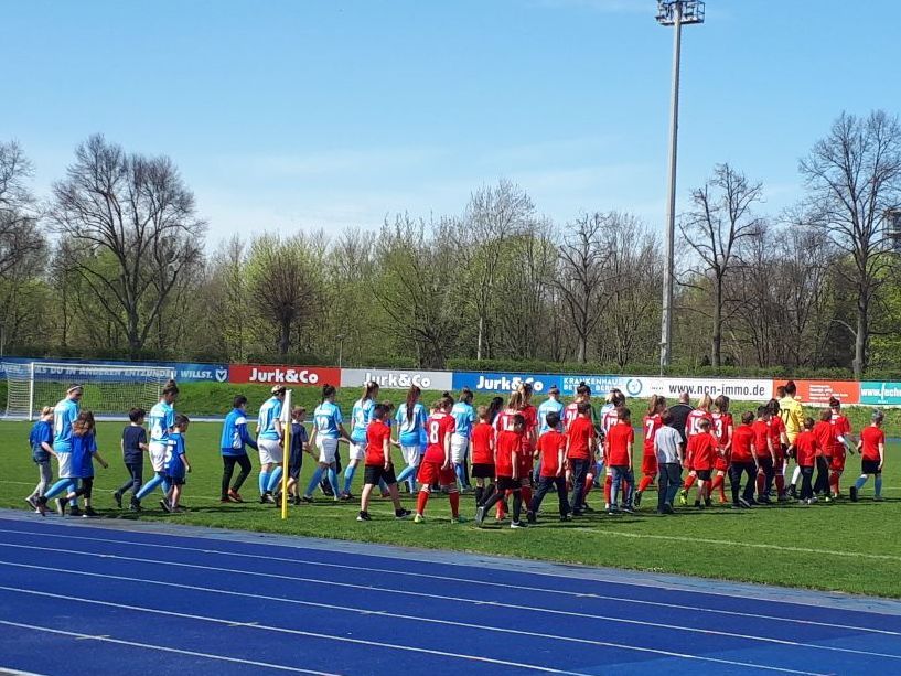 Gruppierung von Kindern in roten und blauen Trikots auf einem Fußballfeld, die sich nach einem Spiel die Hände schütteln.