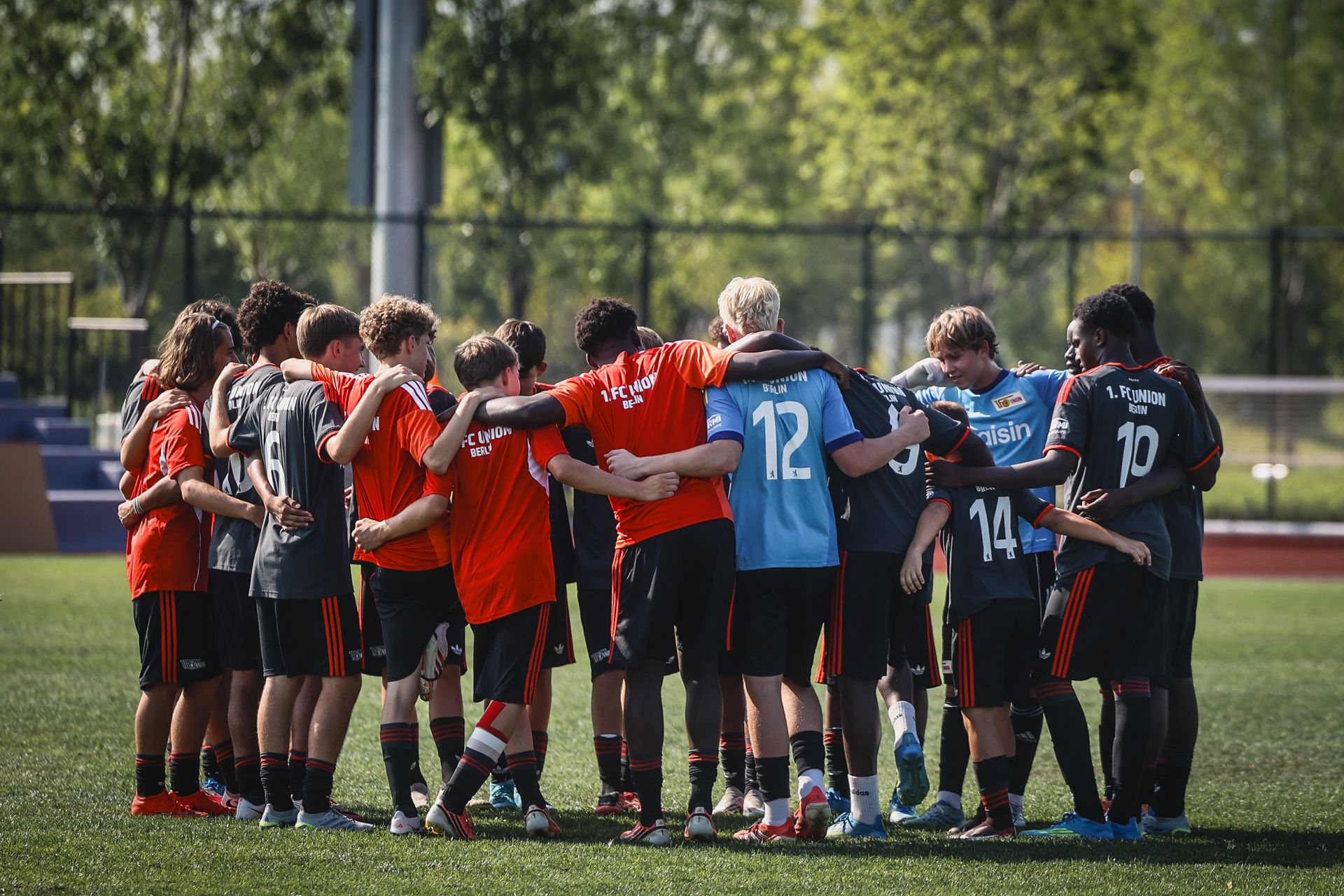 Zwei Gruppen von Fußballspielern stehen sich auf dem Feld gegenüber und bilden einen Kreis, während sie sich umarmen.