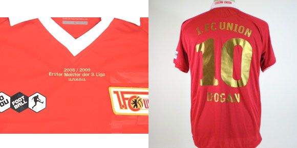 Rotes Trikot mit weißen und goldenen Details, auf der Rückseite die Nummer 10 und den Namen "Dogan".