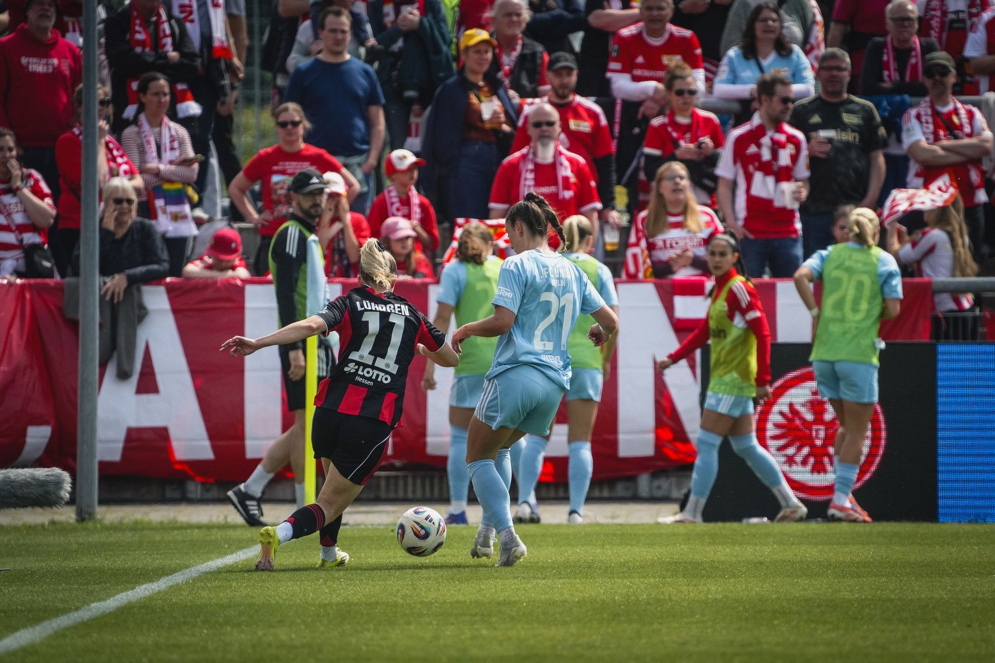 Spielszene im Fußball mit zwei Spielerinnen in Aktion, umgeben von jubelnden Fans im Hintergrund.