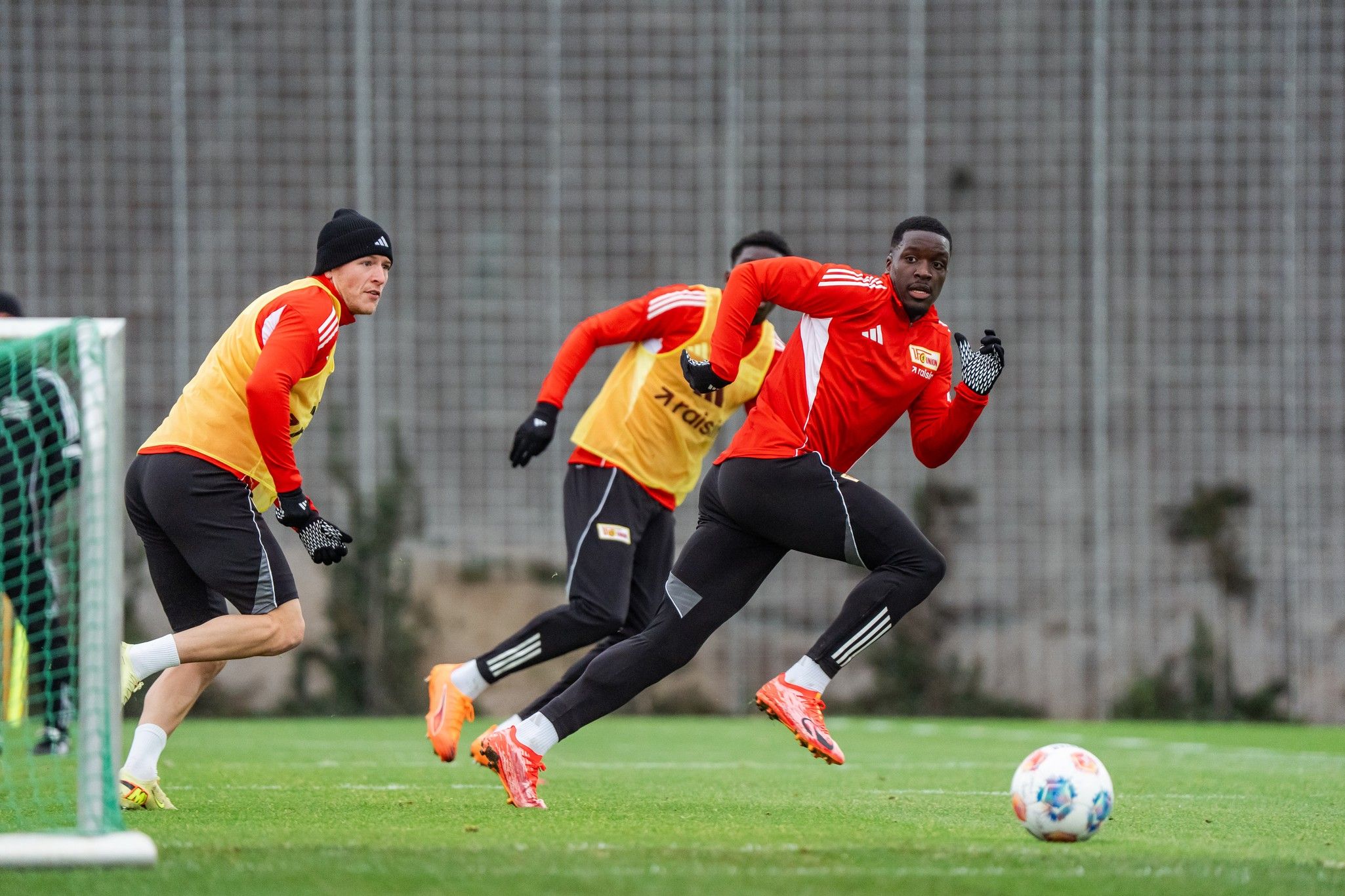 Fußballspieler in roten Trikots trainieren auf dem rasen. Ein Spieler sprintet dem Ball hinterher, während andere beobachten.
