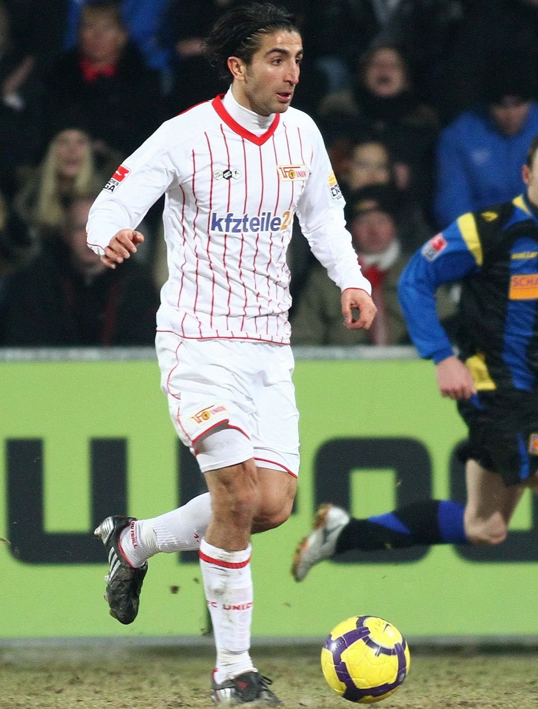 Ein Fußballspieler in einem weißen Trikot mit roten Streifen dribbelt den Ball auf dem Spielfeld.