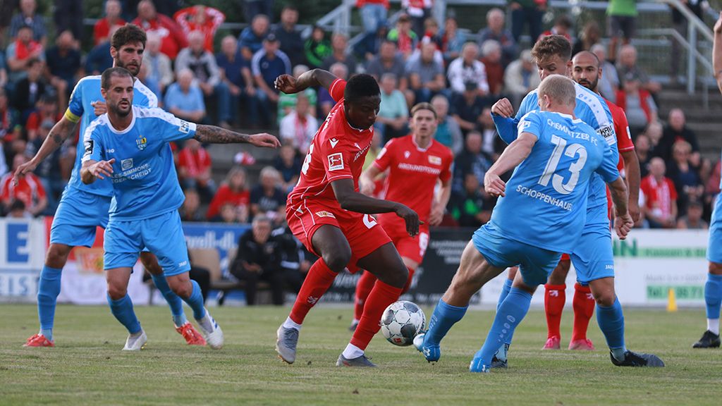 A soccer match scene, two teams in red and blue jerseys battling for the ball on a grass field.
