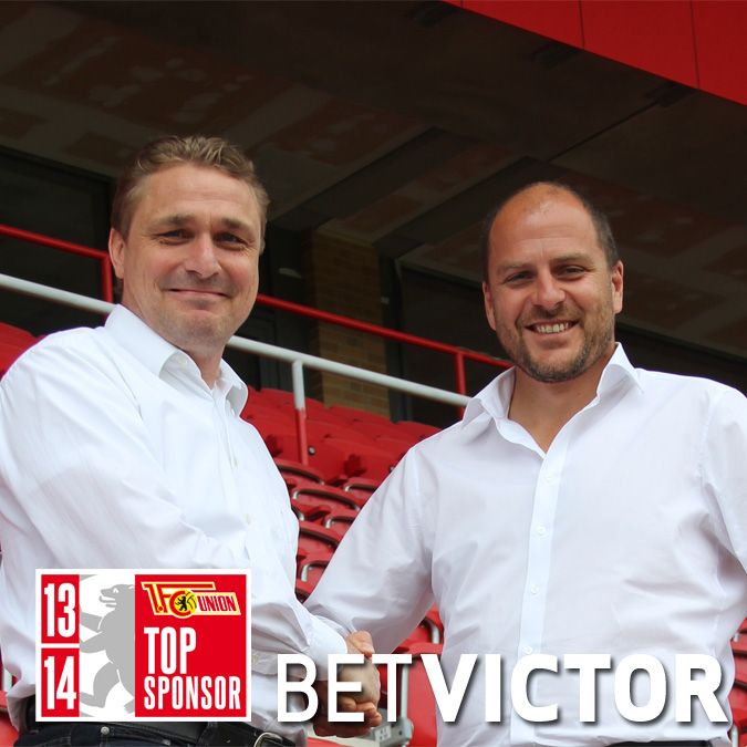 Zwei Männer in weißen Hemden schütteln sich die Hände vor einer Tribüne, mit dem Logo von BetVictor und dem Text "TOP SPONSOR".