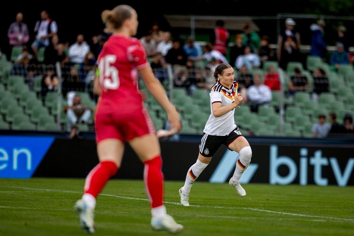 Fußballspiel mit einer deutschen Spielerin, die jubelnd in Richtung der Zuschauer sprintet, während eine gegnerische Spielerin im Hintergrund steht.