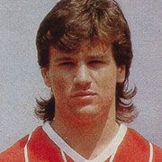 Ein junger Mann mit braunen Haaren in einem roten Fußballtrikot, schaut ernst in die Kamera.