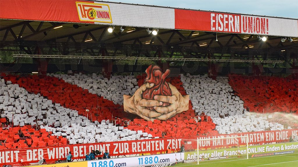 Große Fankurven-Inszenierung mit roten und weißen Schals, die ein Herz in Händen darstellen, im Stadion von Union Berlin.