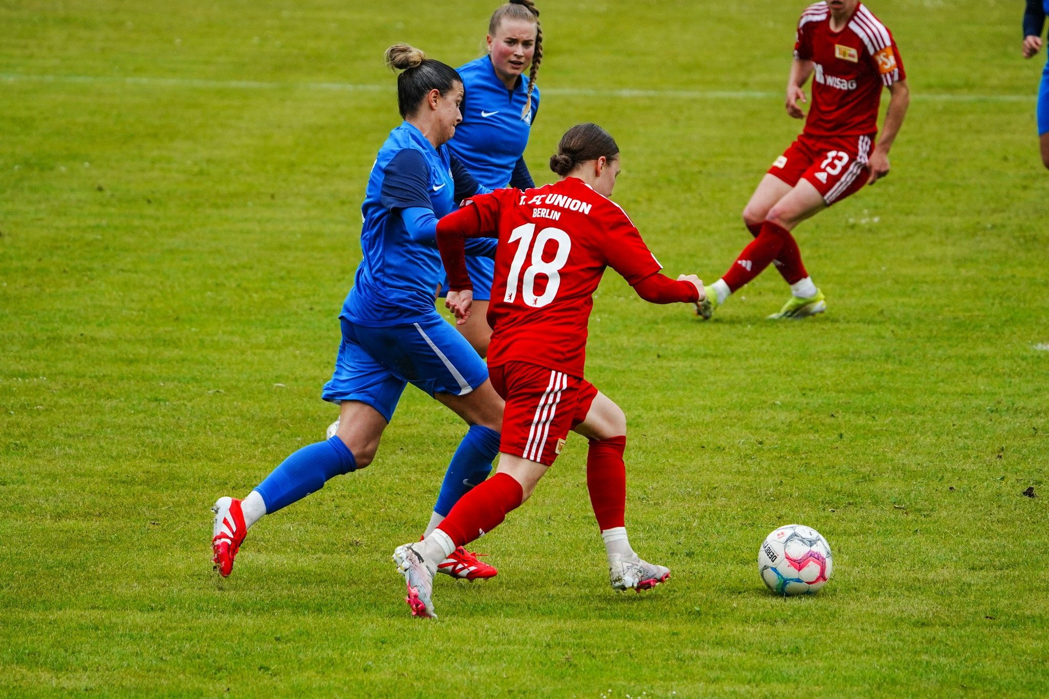 Zwei Fußballspielerinnen im Wettkampf um den Ball auf einem grünen Spielfeld während eines Spiels.