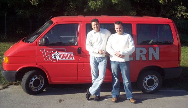 Zwei Männer stehen lächelnd neben einem roten Lieferwagen mit der Aufschrift "H. Union" und "ERN".