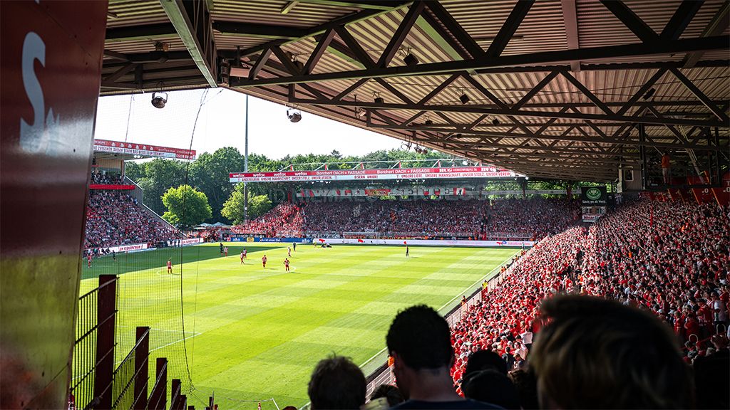 Blick auf ein Fußballstadion mit einer dichten Menge von Fans, die in Rot gekleidet sind, während ein Spiel auf dem Rasen stattfindet.