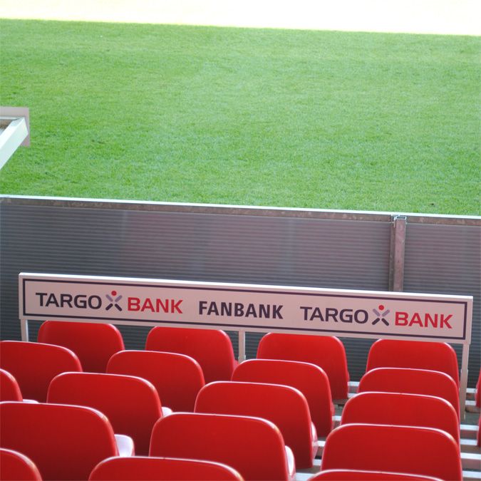 Rote Stadion-Sitze mit einem Schild der TARGO BANK FANBANK im Vordergrund. Rasenfeld im Hintergrund.