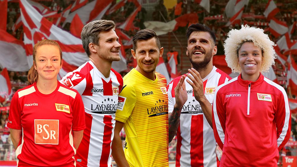 Five soccer players in red-and-white jerseys are standing in a stadium with cheering fans in the background.