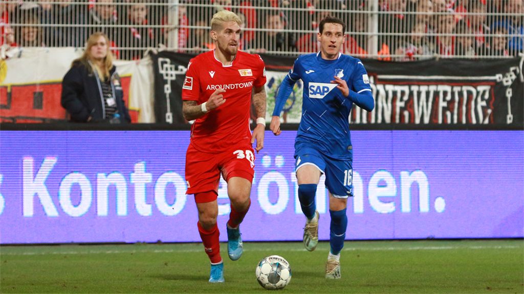 Zwei Fußballspieler auf dem Spielfeld, einer in rotem und der andere in blauem Trikot, während des Spiels in Aktion.