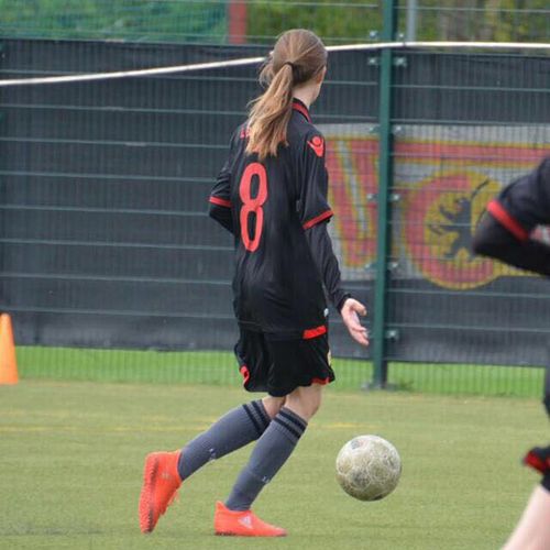 Mädchen in schwarzem Fußballtrikot mit der Nummer 8 dribbelt einen Fußball auf einem Sportplatz.