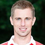 Ein Mann mit blonden Haaren und blauen Augen lächelt in die Kamera, trägt ein rot-weißes Sporttrikot.