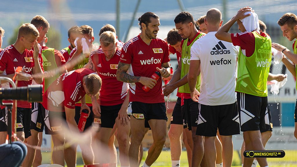 Group training of a soccer team in red jerseys, some players are drinking water, others are chatting on the field.