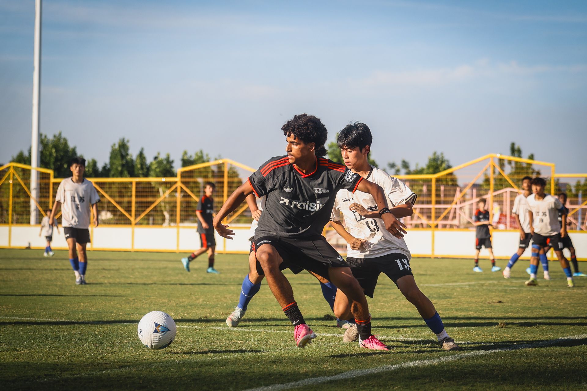 Zwei Jungen spielen Fußball auf einem Platz, einer dribbelt den Ball, während der andere ihn zu stoppen versucht.