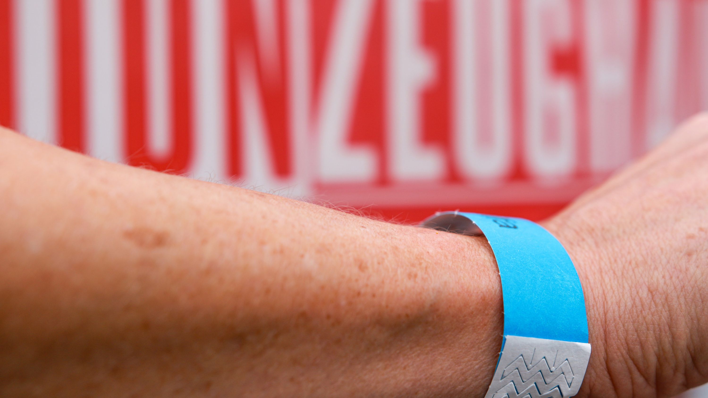 An arm with a blue bracelet in front of a red background with the word "TRAIN".