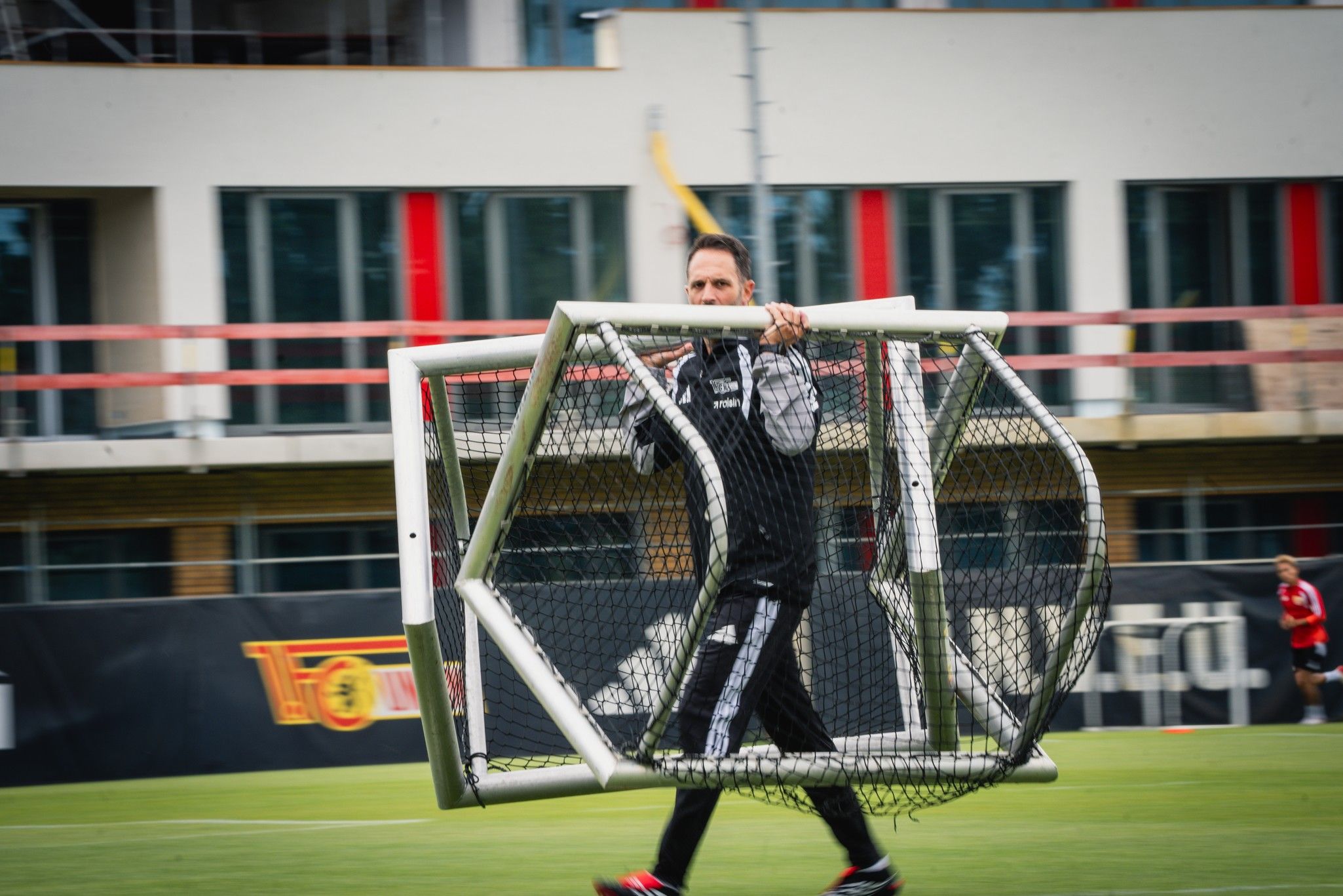 Ein Trainer trägt ein Fußballtor über das Spielfeld während eines Trainings.