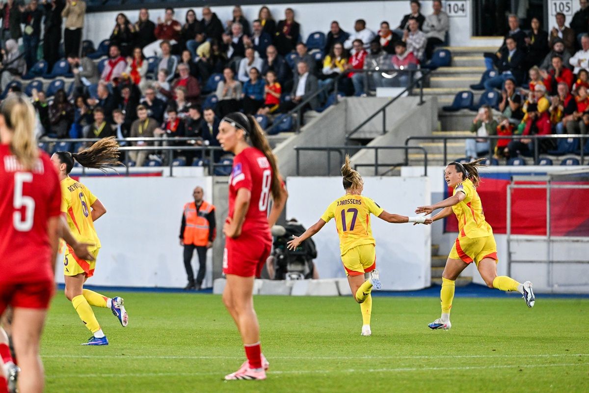 Spielerinnen in gelben Trikots feiern einen Torerfolg auf dem Fußballfeld, Zuschauer im Hintergrund.