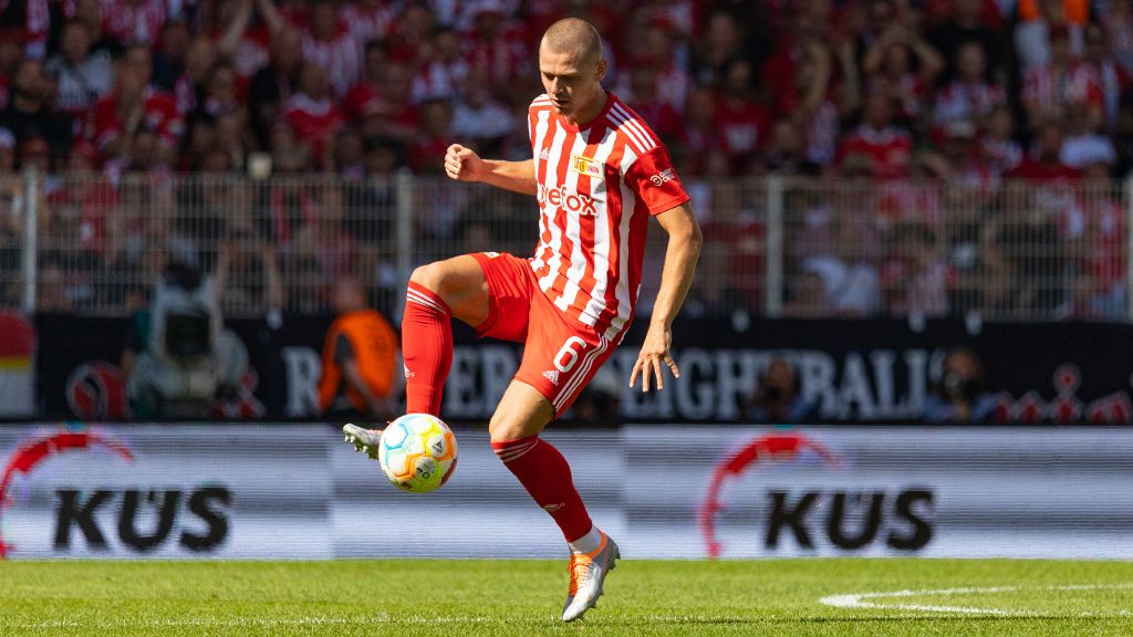 A soccer player in a red and white striped jersey is controlling the ball on the field.