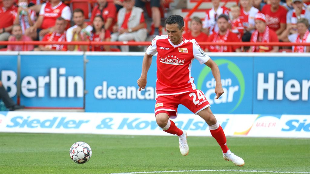 Football player in a red jersey with number 24 dribbling the ball during a game in the stadium. Spectators in the background.
