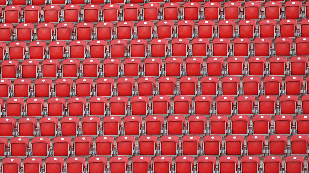 Reihe von roten Stühlen in einem Stadion, gleichmäßig angeordnet und sich wiederholend.