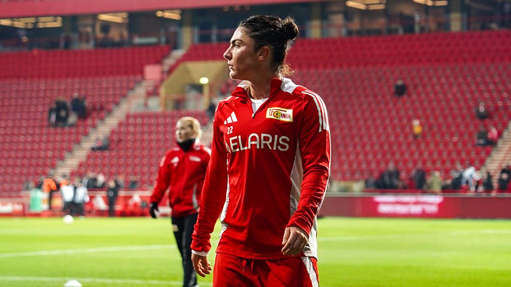 Eine Spielerin von Union Berlin in roter Sportkleidung steht auf dem Spielfeld, während im Hintergrund leere Tribünen zu sehen sind.